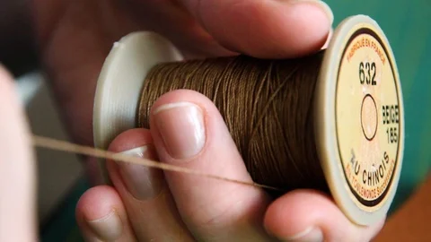Female craftswoman pulling on tan linen thread in leathercraft workshop Stock Footage 87346498