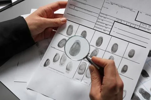 Female criminalist exploring fingerprints with magnifier at table, closeup Stock Photos