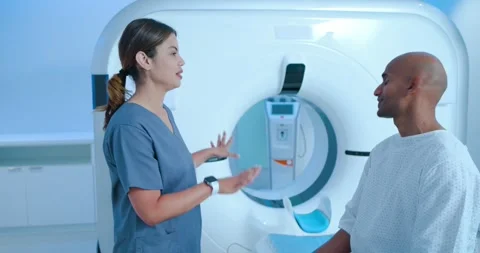 Female CT tech entering placing hand on male patient shoulder pointing at gantry Stock Footage 337025901