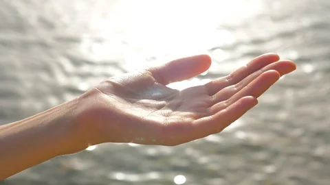Female cupped hand catches falling water drops on seascape background. The sun Video stock 114346309