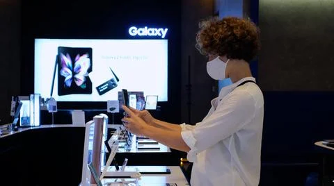 Female customer in face mask testing tacking selfie on new Samsung Galaxy phone Stock Photos
