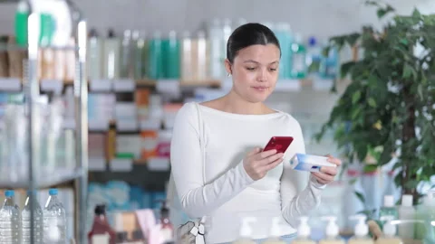 Female customer scanning QR code on box of ointment in pharmacy Stock Footage 319994925