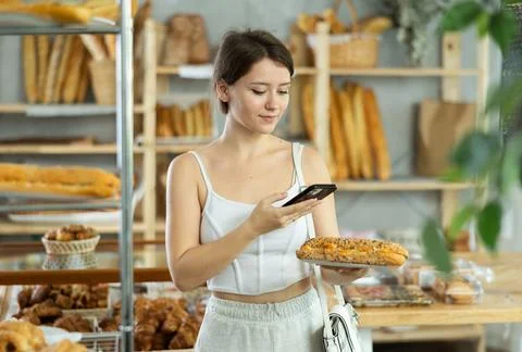 Female customer scanning QR code on label of fresh baked goods in bakery Stockfoto's