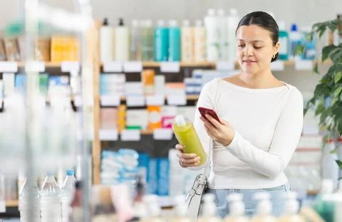 Female customer scanning QR code on bottle on shampoo in store Photos