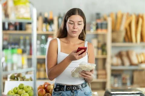 Female customer scans QR code on label oat flakes using smartphone. Checking Foto stock