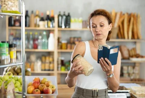 Female customer scans QR code on beans jar label using smartphone. Checking 스톡 사진