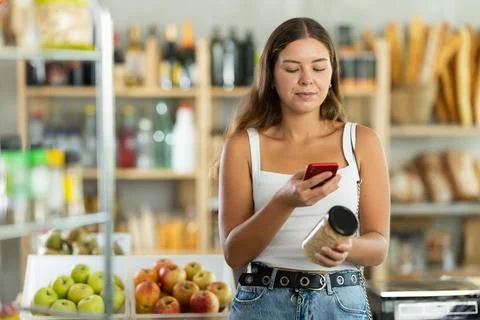 Female customer scans QR code on beans jar label using smartphone. Checking Stock Photos