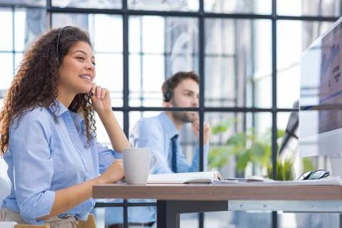Female customer support operator with headset and smiling. Collegue is on the Foto stock