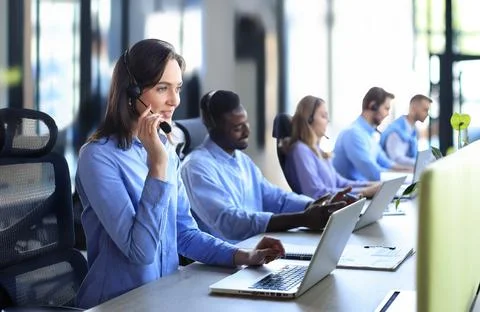 Female customer support operator with headset and smiling, with collegues at Stock Photos