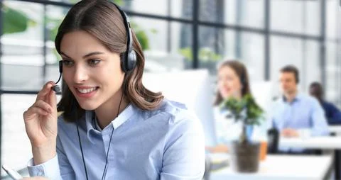 Female customer support operator with headset and smiling, with collegues at Stock Photos