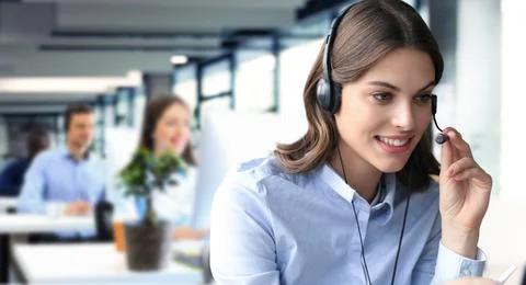 Female customer support operator with headset and smiling, with collegues a.. Stock Photos
