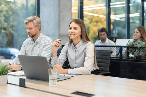 Female customer support operator with headset and smiling, with collegues a.. Stockfoto's