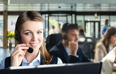 Female customer support operator with headset and smiling, with collegues a.. Stock Photos