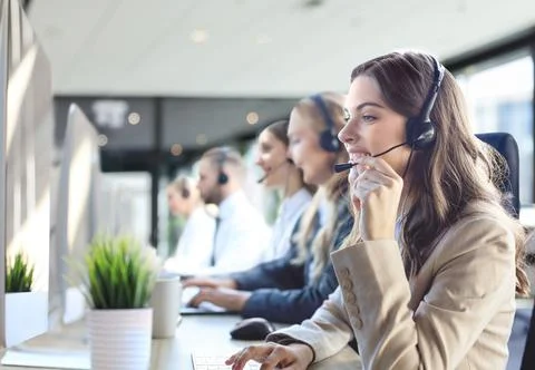 Female customer support operator with headset and smiling, with collegues a.. Stock Photos