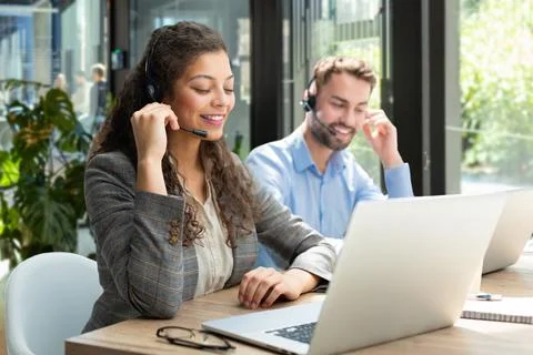 Female customer support operator with headset and smiling, with collegues a.. Stock Photos