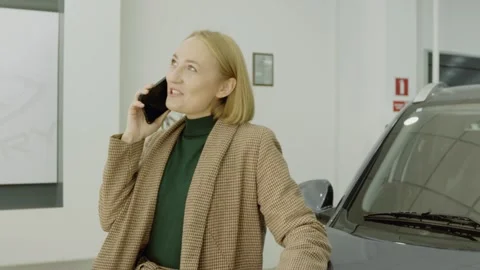 Female customer talking on smartphone while standing in a luxury car showroom Stock Footage 323170126