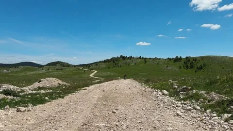Female cyclist rides toward the camera on a gravel road across the Durmitor Stock Footage 344900049