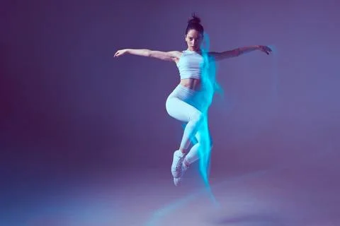 Female dancer jumping in neon studio light performing contemporary dance Stock Photos