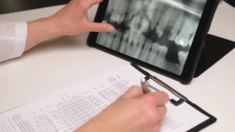 Female dentist looks at x-ray of teeth on a tablet and fills check form. Close Stock Footage