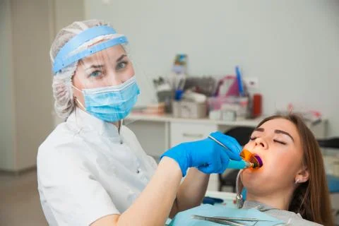 Female dentist work with light-curing seal, patient with caries on chair. Photos
