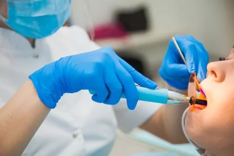 Female dentist work with light-curing seal, patient with caries on chair. Fotos de archivo