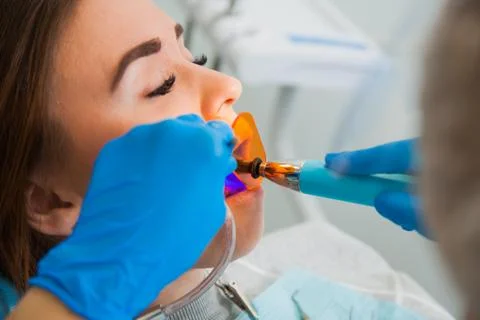 Female dentist work with light-curing seal, patient with caries on chair. 库存照片
