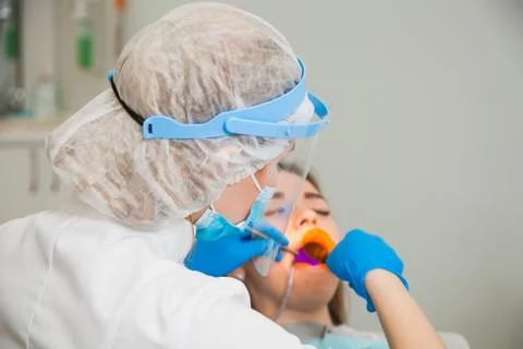 Female dentist work with light-curing seal, patient with caries on chair. 库存照片