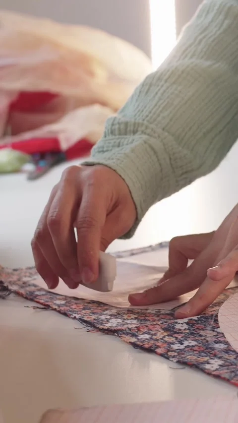 Female designer makes marks using paper patterns on floral print fabric Stock Footage 330052623