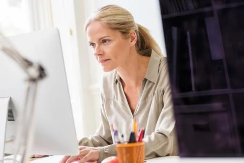 Female designer typing at desktop computer in creative studio 스톡 사진