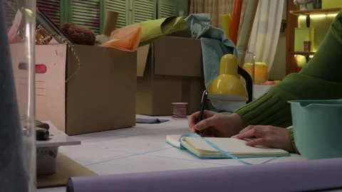 Female designer writing a plan in notebook on messy worktable in creative worksh Stock Footage 328605086