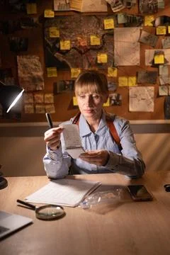 Female detective reading notes sitting near evidence board investigating cr.. Stock Photos