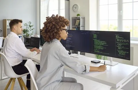 Female developer coding at multi monitor setup in contemporary collaborative Stock Photos
