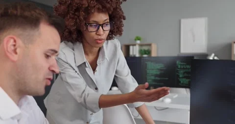 Female developer guiding colleague through code on monitors in modern office Video stock 337928767