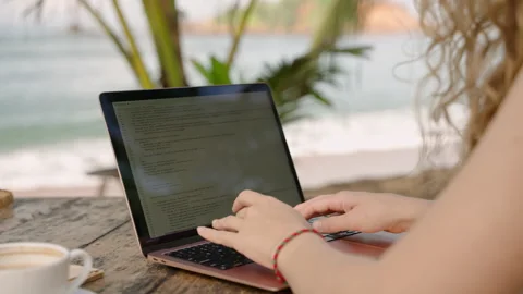 Female developer working on laptop by the ocean. Young woman freelancer coding Stock Footage 234540095