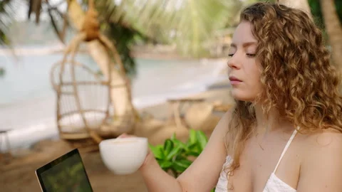Female developer working remotely in an outdoor tropical cafe drinking coffee Stock Footage 241524132