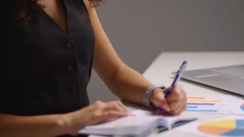 Female dietitian writing notes in planner analyzing nutrition charts at Stock Footage 342477155