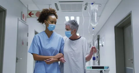 Female diverse doctor and patient wearing face masks walking through hospital Stock Footage