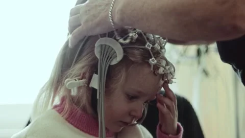 Female doc attaches sensor discs to EEG electrode cap on child head. Medical Stock Footage 326747319
