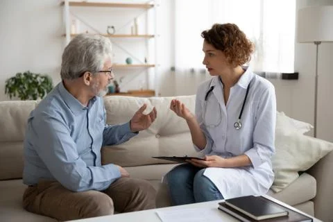 Female doctor consulting senior patient during home medical care visit Stock Photos