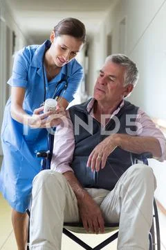 Female doctor giving medicine to senior man in corridor Stock Photos