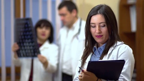 Female doctor holding a folder in his hands. In the background, the doctors Stock Footage 74251553