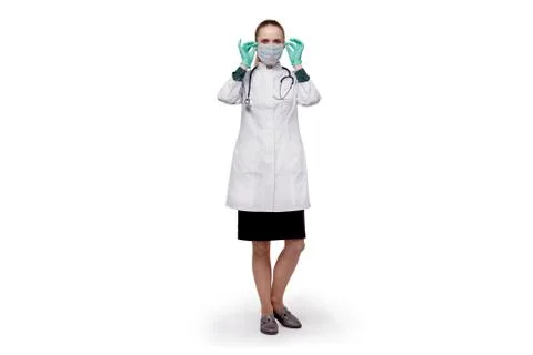 A female doctor, looking at the camera, puts a medical mask on her face. Stock Photos