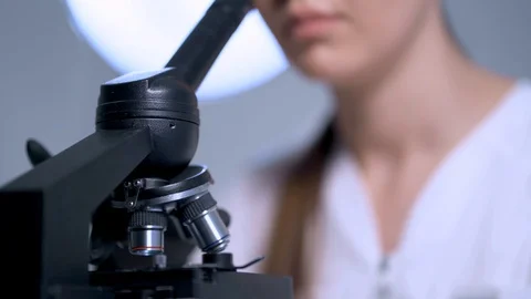 A female doctor looks through a microscope and twists a drum with lenses Stock Footage 128242453