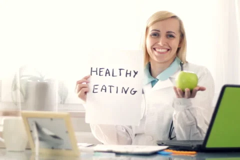 Female doctor in the office holding apple and paper sheet with HEALTHY EATING Stock Footage