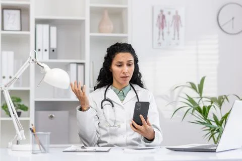 Female doctor with perplexed expression using smartphone Stock Photos
