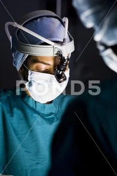 Female doctor in scrubs with head light in surgery Stock Photos