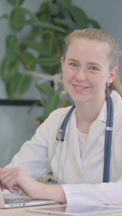 Female Doctor Smiling at Camera while Working on Laptop, vertical video Vídeo Stock 328551394