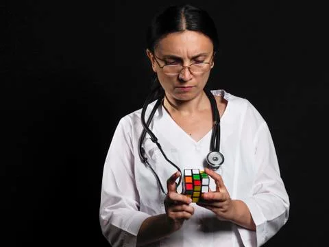 A female doctor solves a complex puzzle by posing on a black background Stock Photos