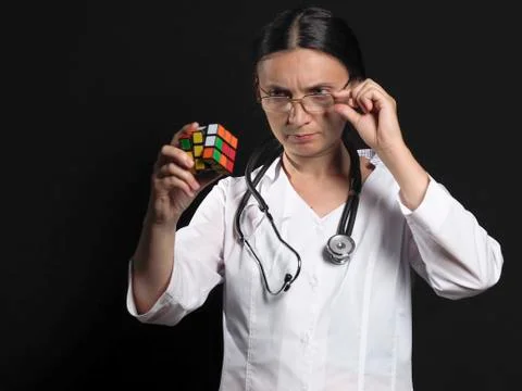 A female doctor solves a complex puzzle by posing on a black background Stock Photos
