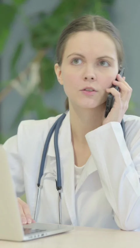 Female Doctor Talking on Phone while using Laptop, vertical video Stock Footage 329108324